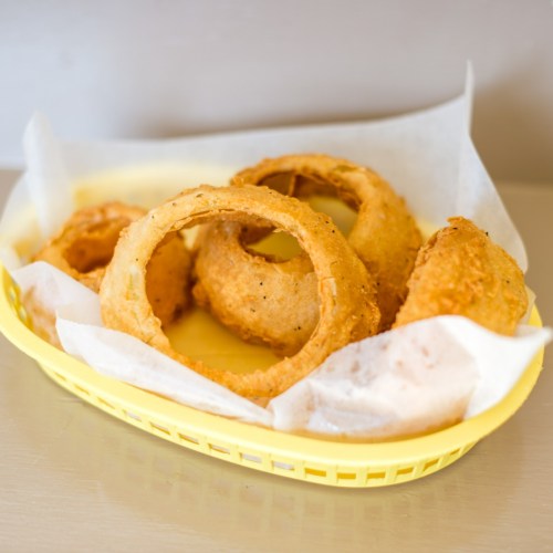 A yellow basket filled with crispy, golden-brown onion rings and a few fried items on parchment paper.