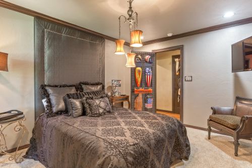 Cozy bedroom featuring a dark bedspread, decorative pillows, stylish lamps, and a wooden chair in a warm, inviting atmosphere.