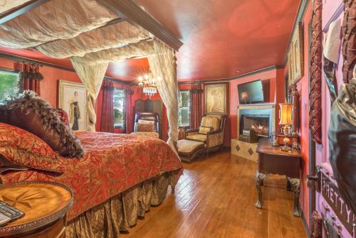 Cozy bedroom with a four-poster bed, elegant decor, a fireplace, and rich red walls.