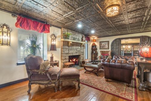 Cozy living room with a stone fireplace, ornate ceiling, leather furniture, and warm lighting.