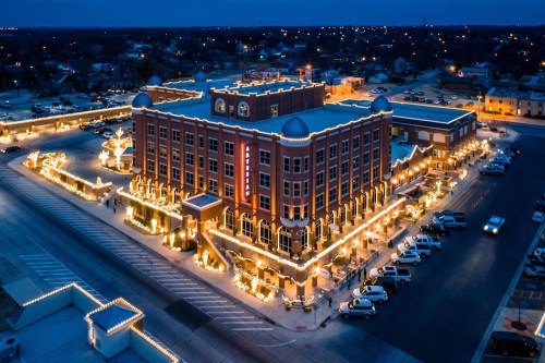 Aerial view of a beautifully lit building at night, surrounded by festive lights and parked cars.