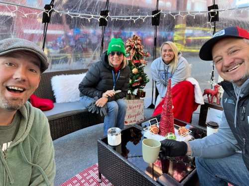 A group of four people smiling in a festive setting with a small Christmas tree and decorations.