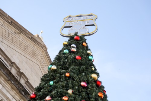 A decorated Christmas tree topped with a sign reading "Sapulpa Route 66" against a clear blue sky.