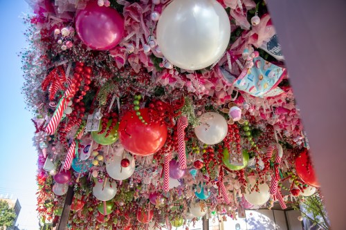 Colorful holiday decorations featuring red, pink, and white ornaments, candy canes, and ribbons hanging from above.