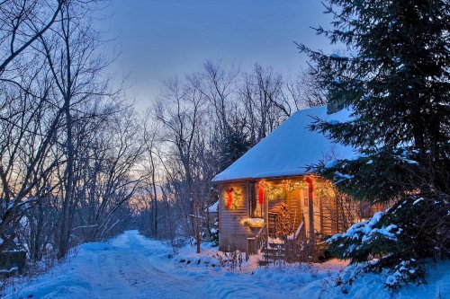 A cozy house decorated with Christmas lights, surrounded by snow-covered trees and a quiet winter landscape at dusk.