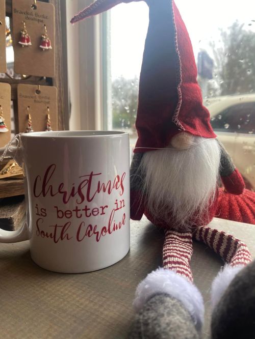 A festive mug reading "Christmas is better in South Carolina" next to a gnome with a red hat and striped legs.
