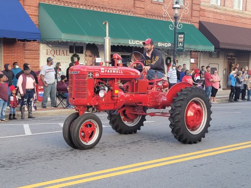 A man rides a red Farmall tractor down a street lined with spectators during a parade.