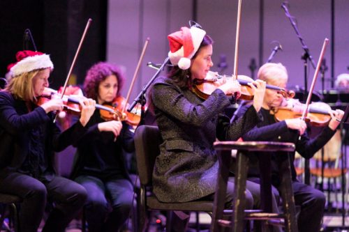 A group of musicians in festive hats playing violins on stage during a performance.