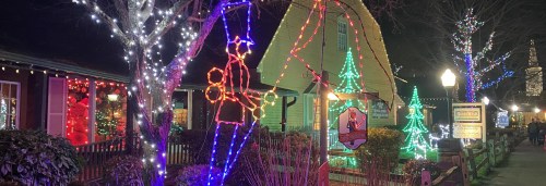 Colorful holiday lights decorate a festive street scene with trees and a whimsical figure holding a gift.