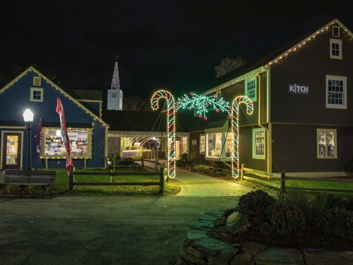 A festive scene featuring a building decorated with Christmas lights and candy cane arches at night.