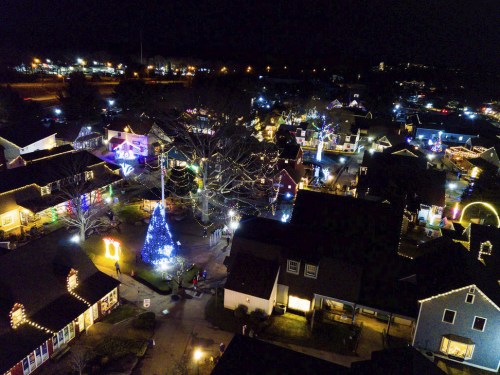 Aerial view of a festive village at night, adorned with colorful Christmas lights and a decorated tree.