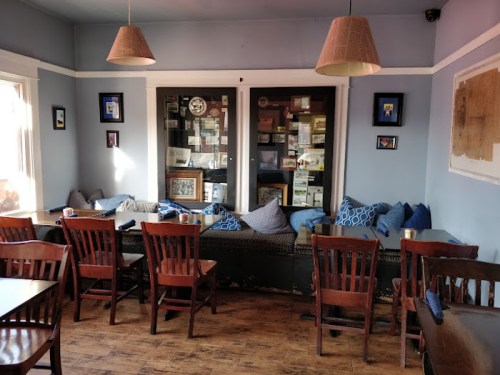 Cozy café interior with wooden chairs, a cushioned seating area, and framed artwork on the walls.
