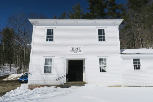 White two-story building with "Orange Town House" sign, surrounded by snow and trees under a clear blue sky.