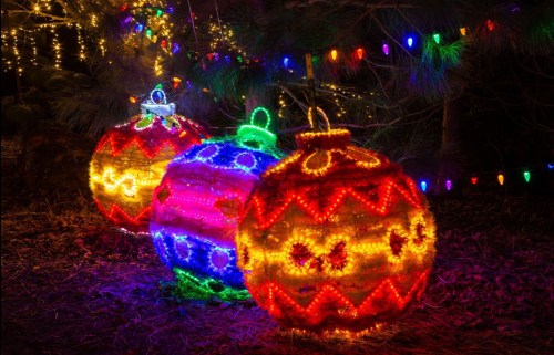 Colorful illuminated Christmas ornaments surrounded by festive lights in a dark outdoor setting.