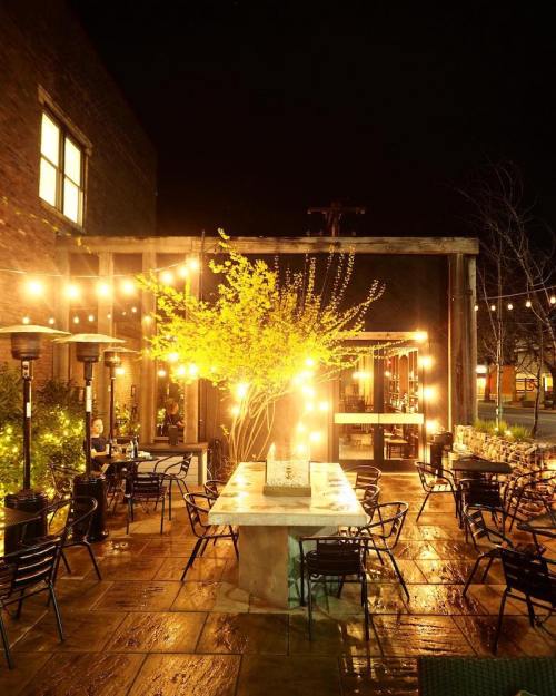 A cozy outdoor dining area at night, illuminated by string lights and featuring a table surrounded by chairs.