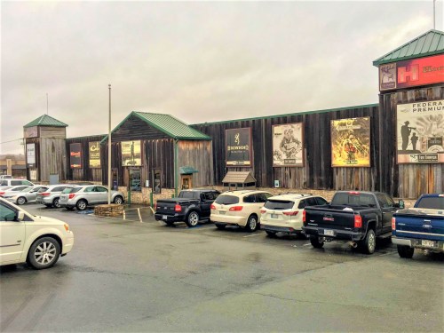 A rustic wooden building with various signs, surrounded by parked cars on a cloudy day.