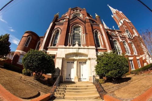 Historic brick church with tall spires, large windows, and a grand entrance, set against a clear blue sky.