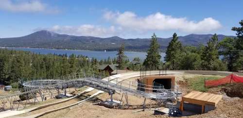 A scenic view of a mountain coaster track overlooking a lake and forested hills under a blue sky.