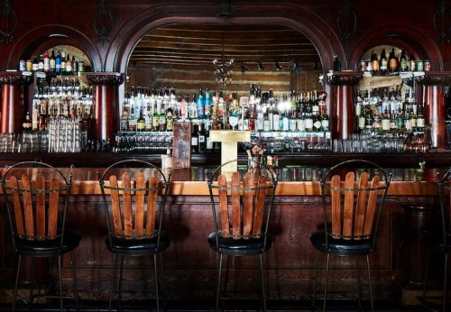 A vintage bar with wooden stools, a mirrored back, and shelves lined with various bottles of liquor.