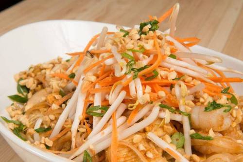 A close-up of a vibrant noodle dish topped with carrots, bean sprouts, and crushed peanuts in a white bowl.
