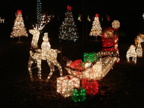A festive display of illuminated holiday decorations, including a reindeer, snowman, Santa, and colorful gift boxes.
