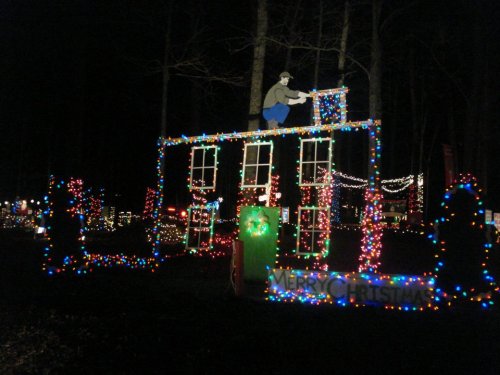 A festive display of Christmas lights featuring a house outline and a figure on the roof, surrounded by colorful decorations.