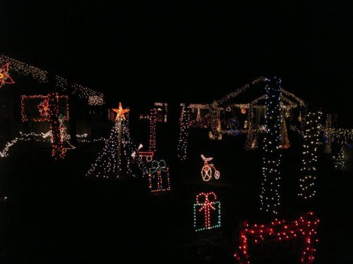 A festive display of colorful Christmas lights and decorations in a dark neighborhood, featuring stars and gift shapes.