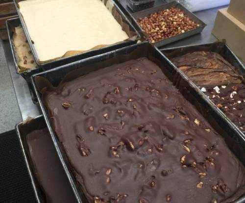 Trays of various fudge types, including chocolate and vanilla, with nuts and toppings visible.