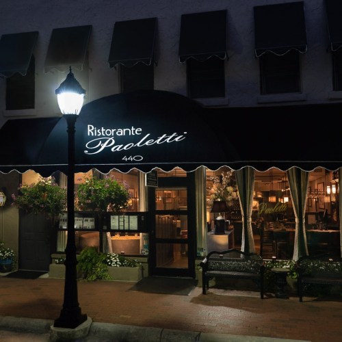 A cozy restaurant entrance at night, featuring a sign that reads "Ristorante Paoletti" and decorative plants.