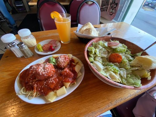 A table with a plate of spaghetti and meatballs, a salad, bread, and a drink in a casual dining setting.