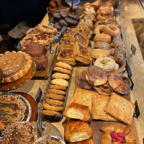 A variety of baked goods displayed on a wooden table, including pastries, cookies, donuts, and cakes.