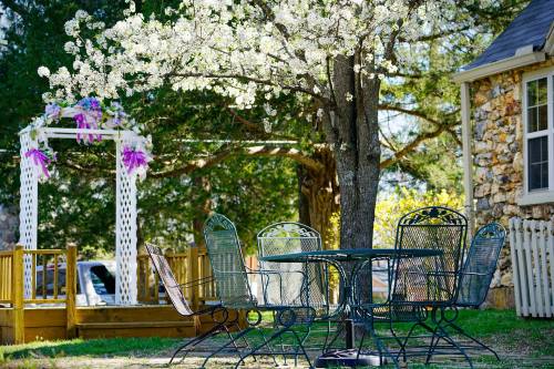A charming outdoor scene with a flowering tree, a table and chairs, and a white gazebo adorned with purple decorations.