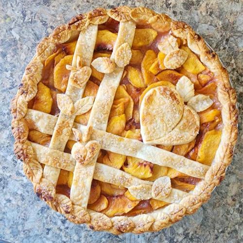 A beautifully baked peach pie with a lattice crust and decorative leaf and heart shapes on top.