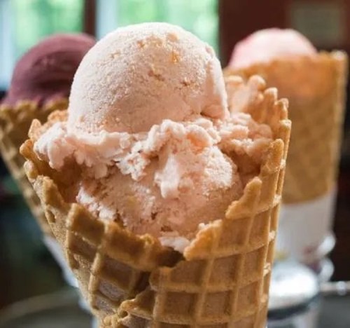 Three ice cream cones with scoops of pink and purple ice cream, set against a blurred background.