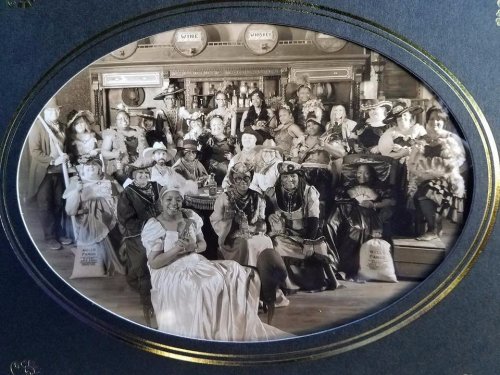 A large group of people in historical costumes, posing together in a vintage setting, with various props and expressions.