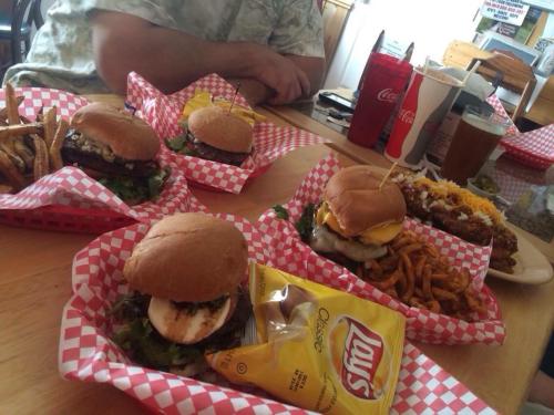 A table with several burgers in red checkered baskets, fries, and drinks, including soda and iced tea.