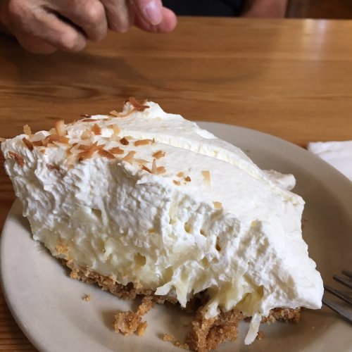 A slice of coconut cream pie topped with whipped cream and toasted coconut on a plate.