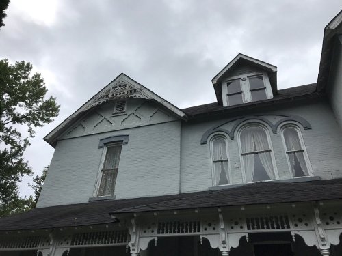 Victorian-style house with gray brick, ornate trim, and cloudy sky above.