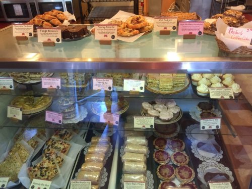 A display case filled with various baked goods, including brownies, pastries, and cakes, all labeled with names.