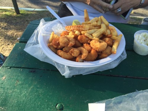 A plate of fried shrimp and crinkle-cut fries, served with a side of coleslaw and lemon wedges.