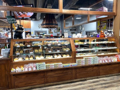 A bakery display case filled with various baked goods, including cakes, pastries, and snacks, in a cozy shop setting.