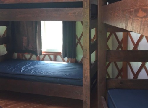 Two wooden bunk beds in a cozy room with a window and dark curtains.