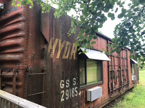 A weathered shipping container converted into a small building, surrounded by greenery.