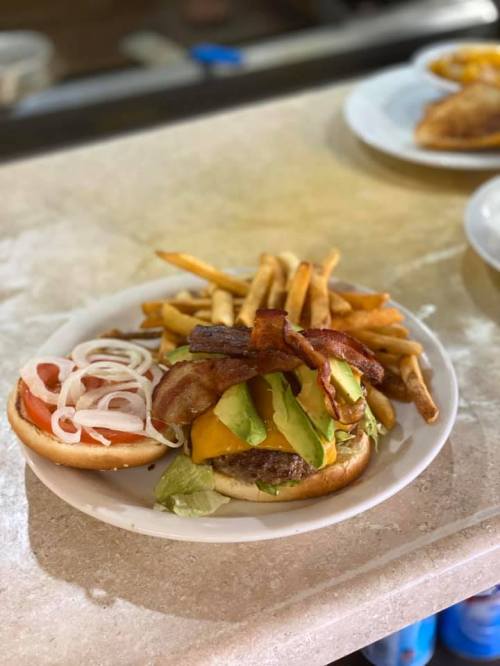 A plate with a burger topped with bacon, lettuce, tomato, and onions, served with a side of crispy French fries.