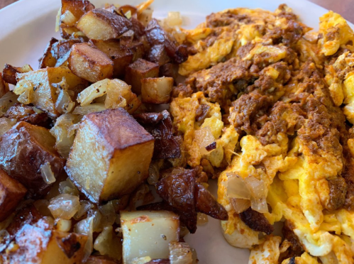 A plate of scrambled eggs mixed with ground meat, served alongside crispy diced potatoes and onions.