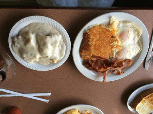 A breakfast plate with eggs, bacon, hash browns, and a side of biscuits and gravy on a table.