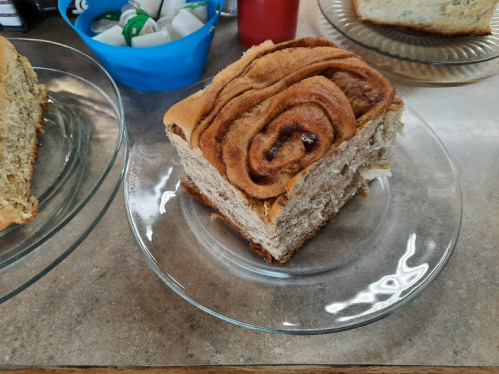 A slice of cinnamon roll bread on a glass plate, with a soft, swirled top and a light brown crust.