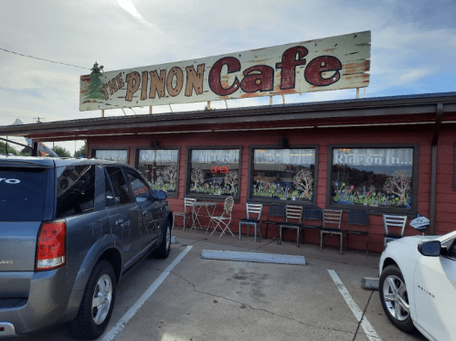 Exterior of the Pinon Cafe with a sign, parked cars, and colorful window decorations.