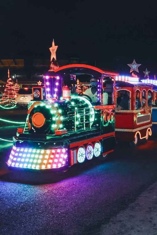 A brightly lit train decorated with colorful lights, traveling through a festive night scene with star decorations.