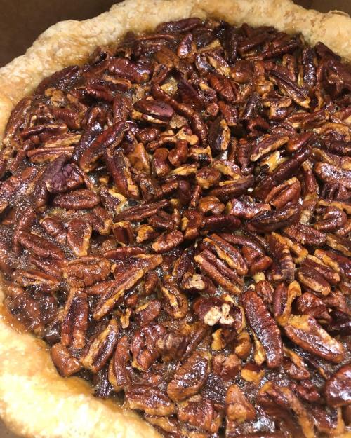 A close-up of a pecan pie with a golden crust and a glossy, nut-covered filling.